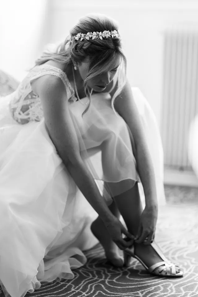 La mariée attache sa sandale pendant les préparatifs, en noir et blanc – Frédéric Leroux, photographe de mariage à Reims