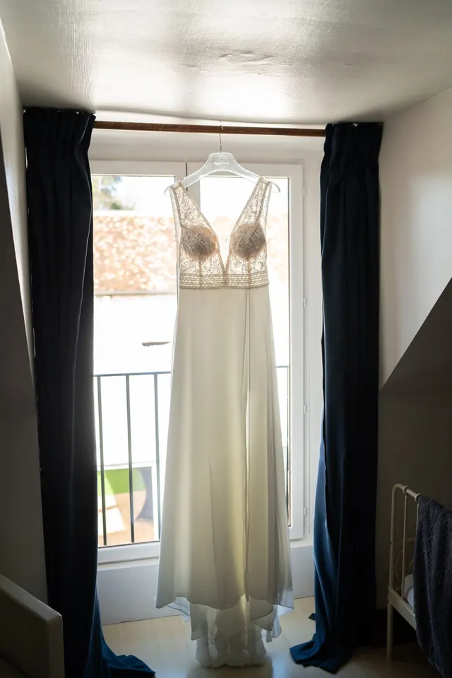 Robe de mariée suspendue devant une fenêtre – Frédéric Leroux, photographe de mariage à Reims