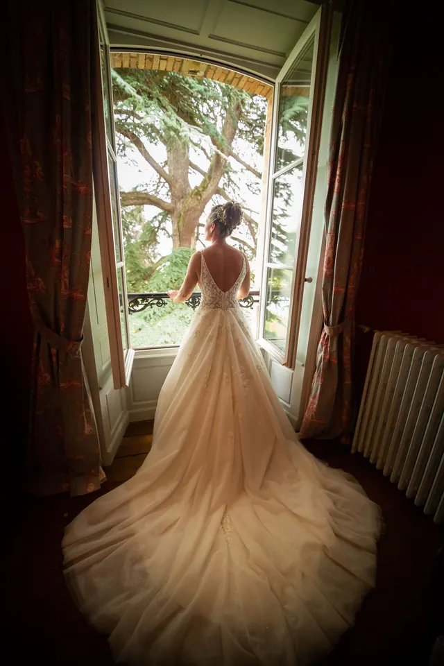 Mariée de dos, longue traîne devant une fenêtre – Frédéric Leroux, photographe de mariage à Reims